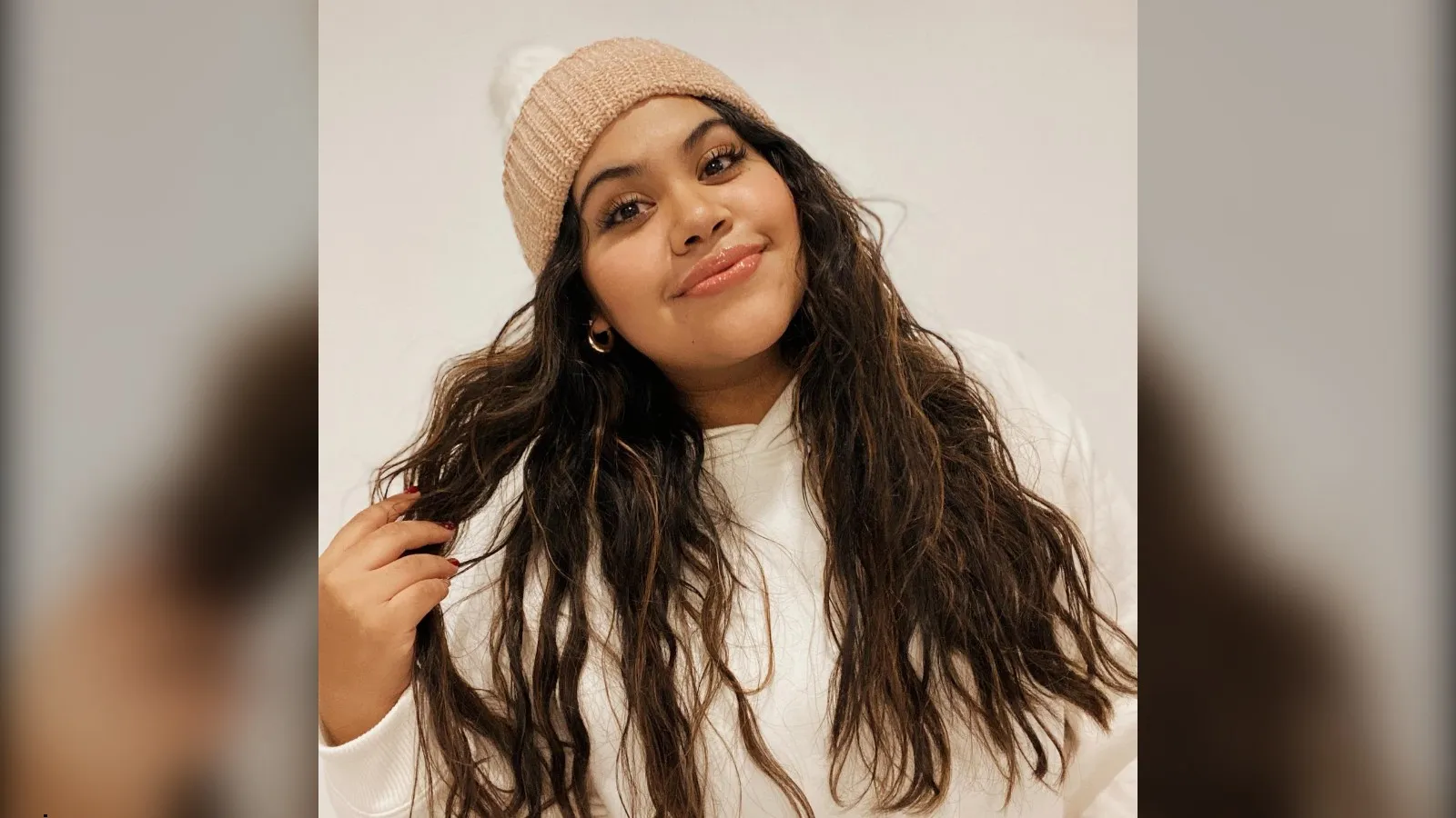 Woman with long loose waves wearing a beige pom pom beanie, beanie hairstyle