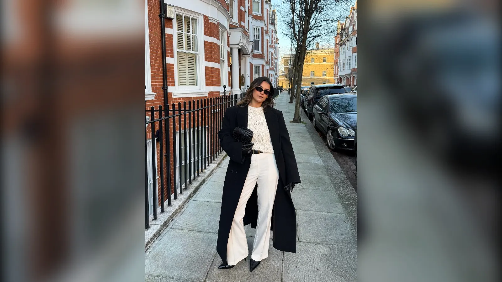 Woman in a black wool coat, cream sweater and cream wide leg pants walking on a city street
