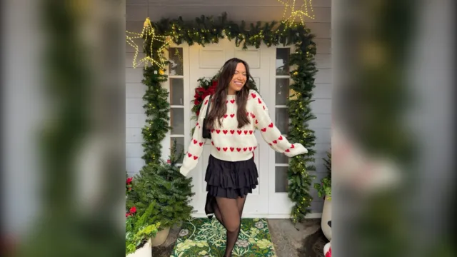 Woman in a cream sweater with red hearts, a black ruffle mini skirt and sheer tights by a decorated door
