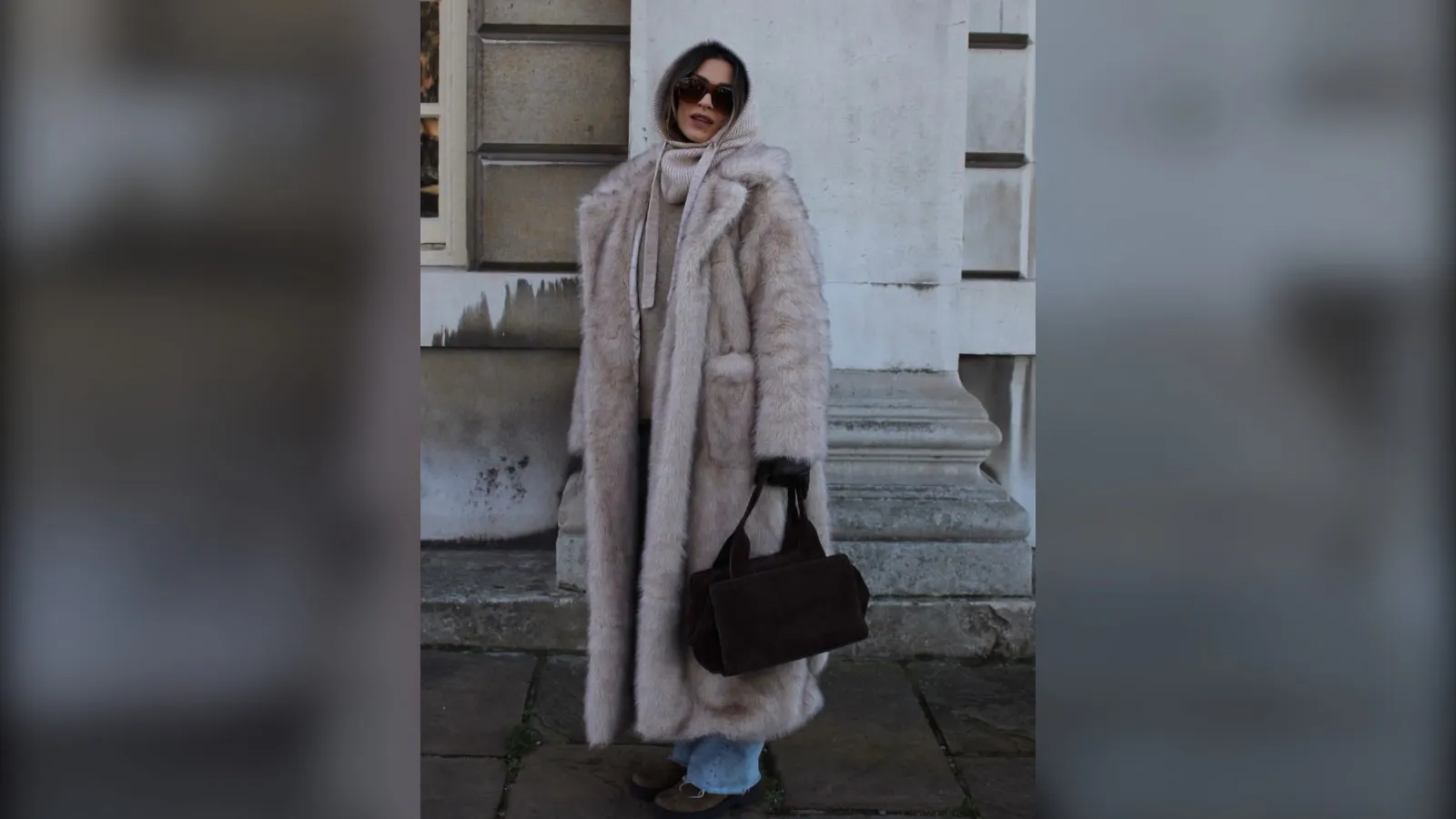 Woman in a long pale faux fur coat with a scarf over her head, jeans and a black bag