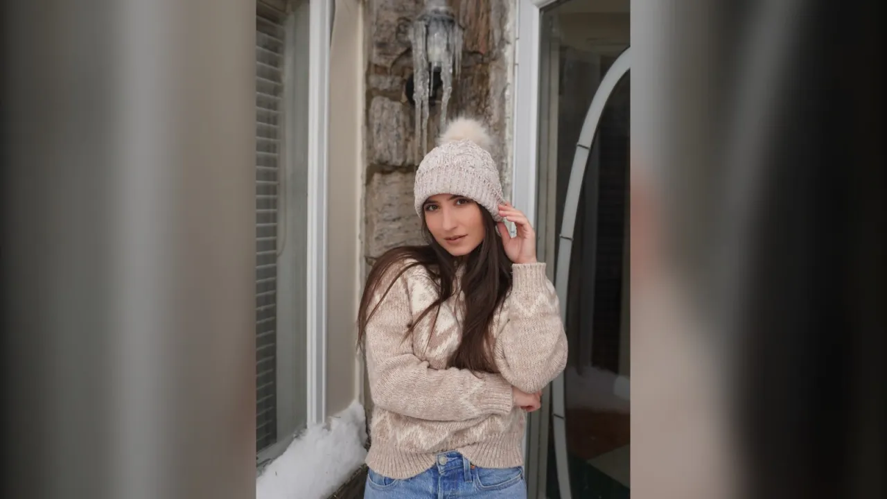 Woman in a cream pom beanie and oatmeal cable knit sweater on a snowy day
