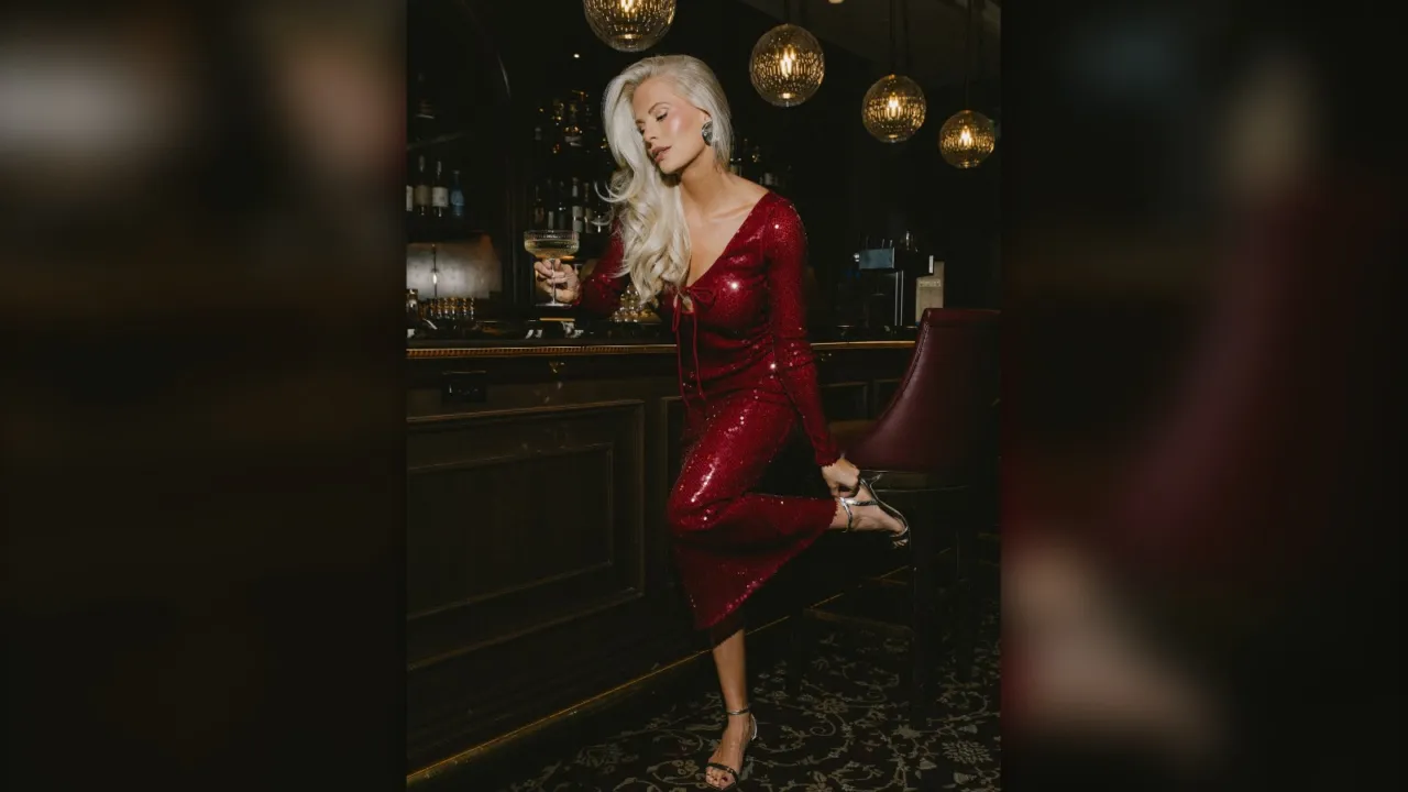 Woman in a red sequin long sleeve midi dress holding a drink at a dark cocktail bar