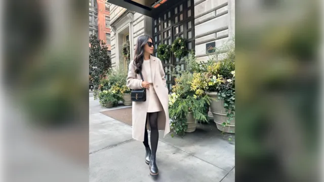 Woman in a cream long coat, black leggings and ankle boots on a city street