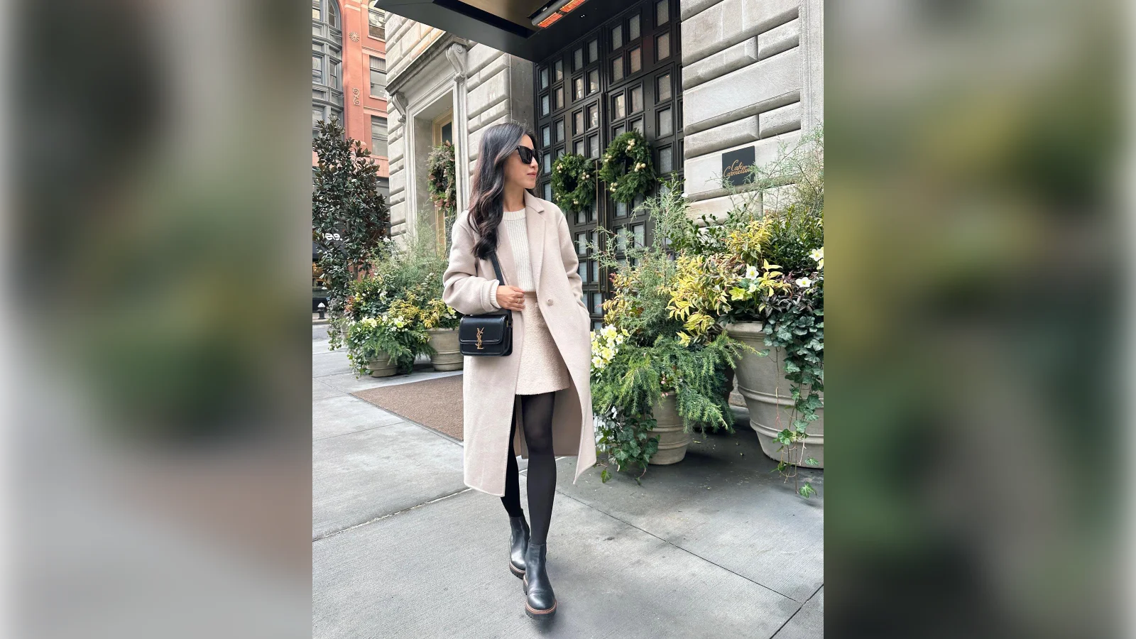 Woman in a cream long coat, black leggings and ankle boots on a city street