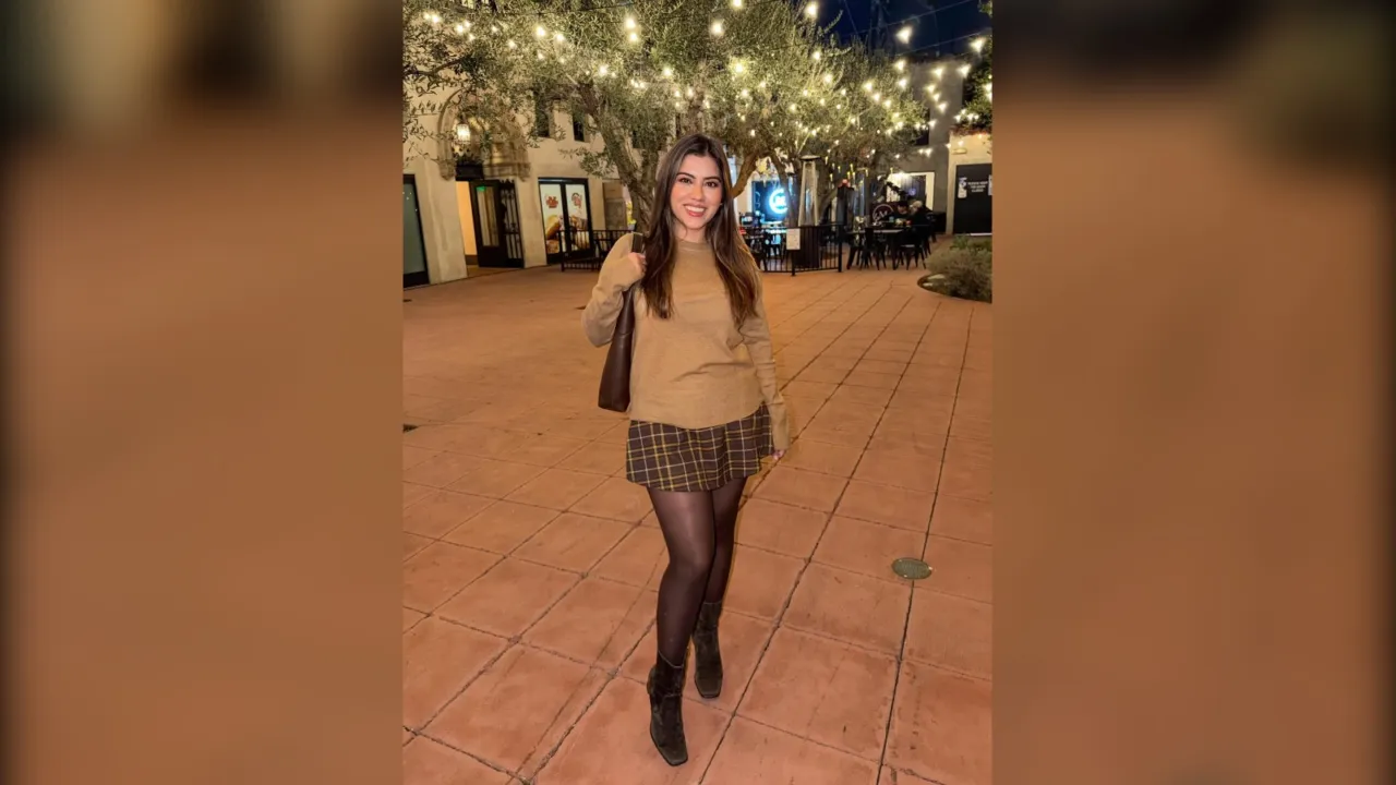 Woman in a camel sweater, brown plaid mini skirt, sheer tights and boots under string lights