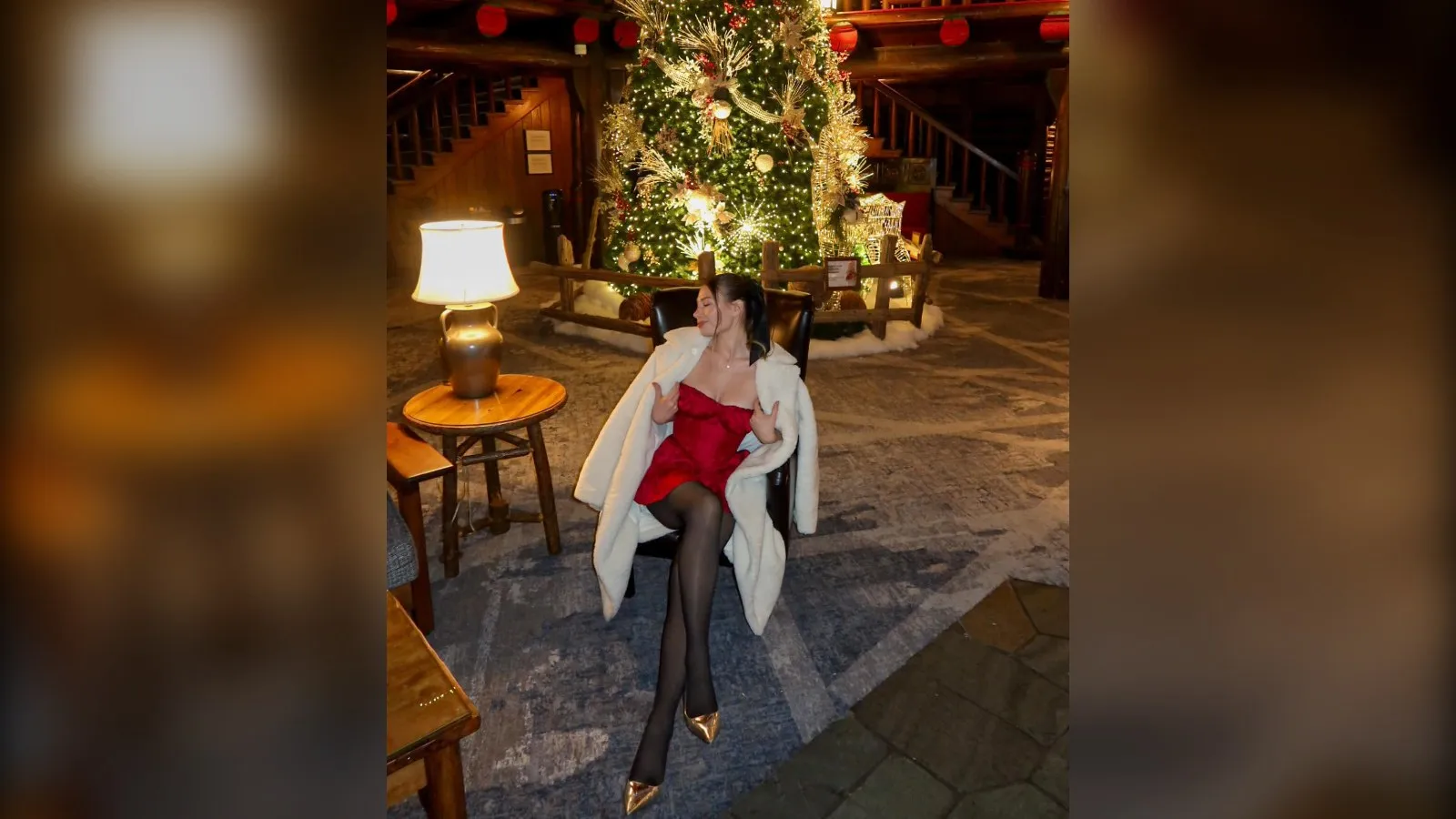 Woman in a short red dress, black tights and a white faux fur coat by a Christmas tree, red Christmas outfit