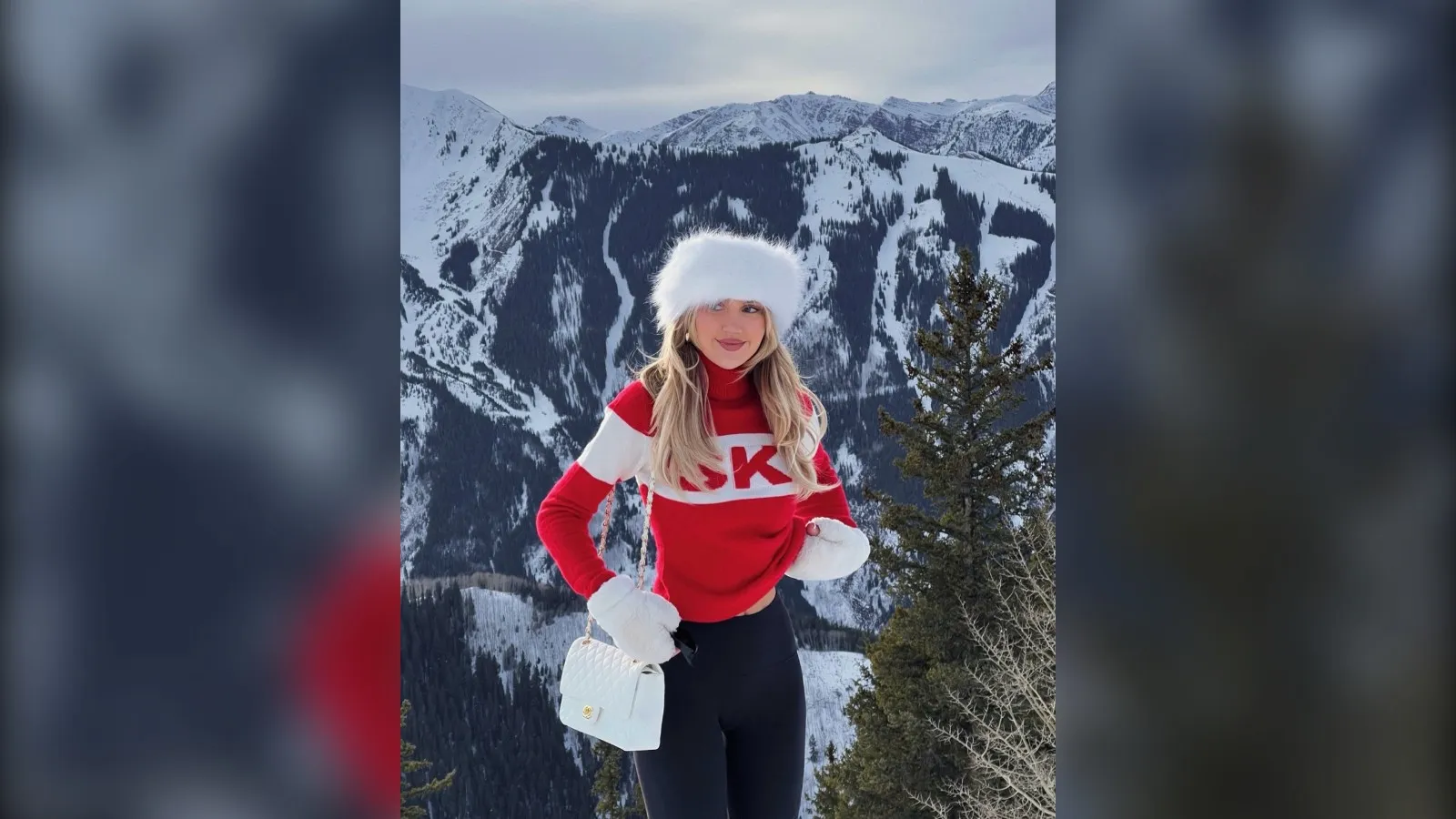 Woman in a red ski sweater, black ski pants and a white fur hat on a snowy mountain in Aspen
