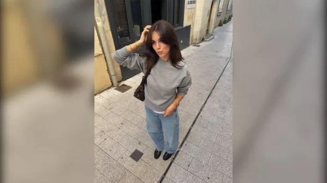 Woman in a gray crew neck sweater and straight jeans on a city street