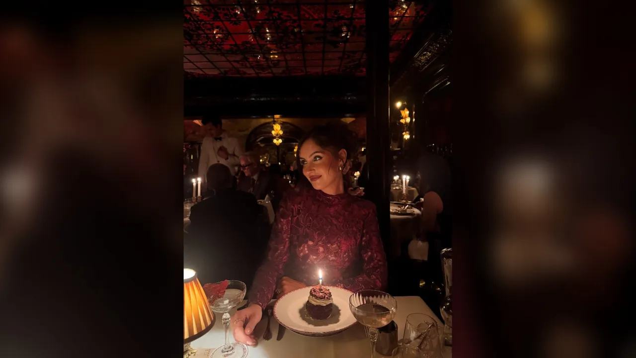Woman in a red sequin top smiling at a birthday cake with a candle at dinner